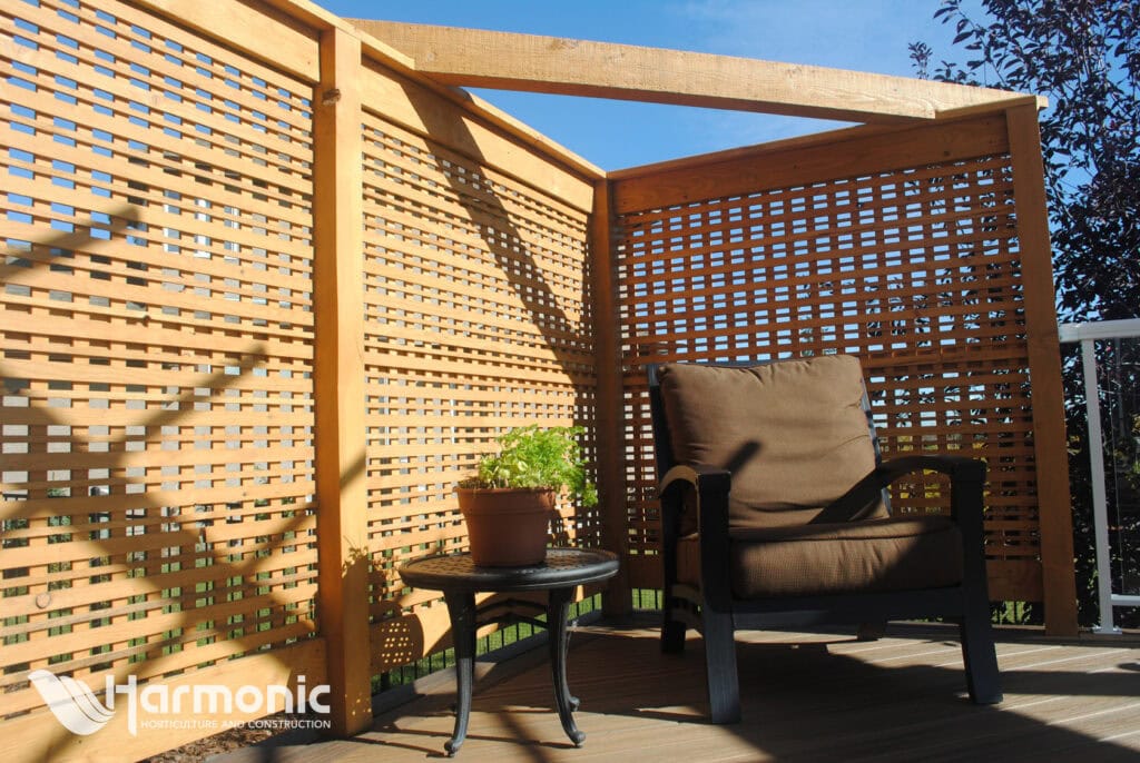 Wooden lattice patio screen enclosing a deck corner with cushioned chair and small table.