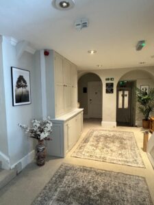 Hallway with light walls, recessed lighting, rugs, vase, tree picture, doors, and exit signs.