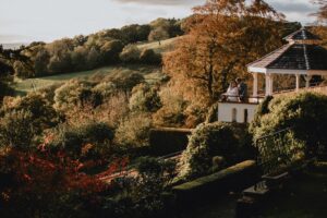 Couple on gazebo overlooking a lush, autumn landscape with trees and hills in golden light.