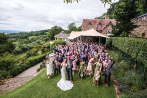 Group celebrating on a lawn with countryside views and a tented area in front of a house.