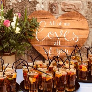 Heart-shaped wooden sign with a romantic message, flowers, and iced fruit drinks on trays.