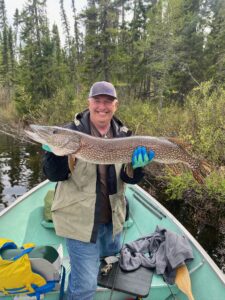 Person in a boat holding a large fish, surrounded by forest and fishing gear.