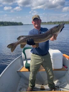 Person on a boat holding large fish with lake, trees, cloudy sky in background