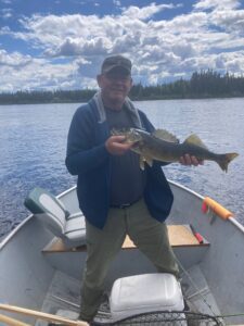 Person in boat holds fish on lake with forested shore and partly cloudy sky.