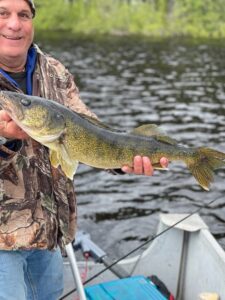 Person in camouflage jacket holding large fish on boat with water background.