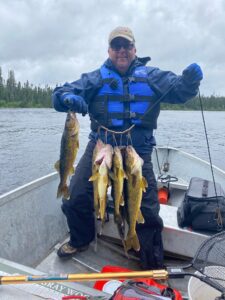 Person in life jacket on boat holding stringer of fish on a lake with a wooded background.