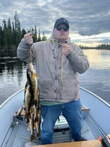 Person on boat holding a string of fish, with lake and forest in the background under cloudy sky.
