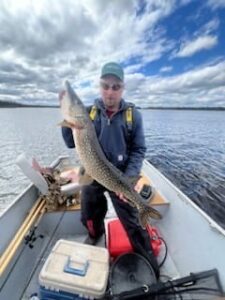 Person on lake boat holding large fish, surrounded by fishing gear, under a partly cloudy sky.
