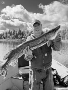 Person in a boat on a lake holding a large fish, forest and cloudy sky background, black and white