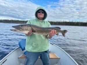 Person in a hooded sweatshirt and sunglasses holding a large fish on a boat in a lake.