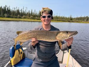 Person on a boat holding a large fish, with trees and clear sky in the background.