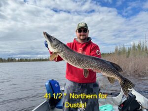 Person on a boat holds a 41.5-inch northern pike, lake and cloudy sky in the background.