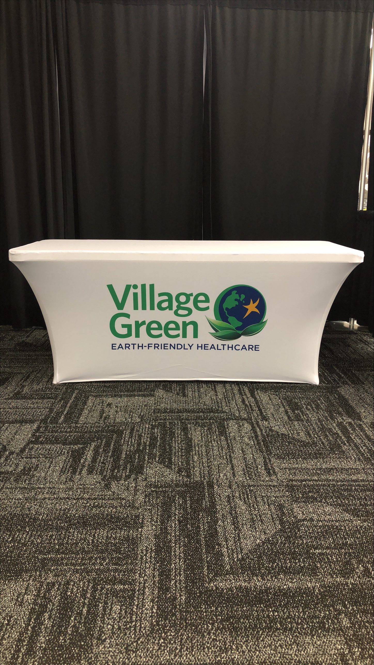 A custom tablecloth featuring the company's logo printed on white, fitted to hold tight to the table.