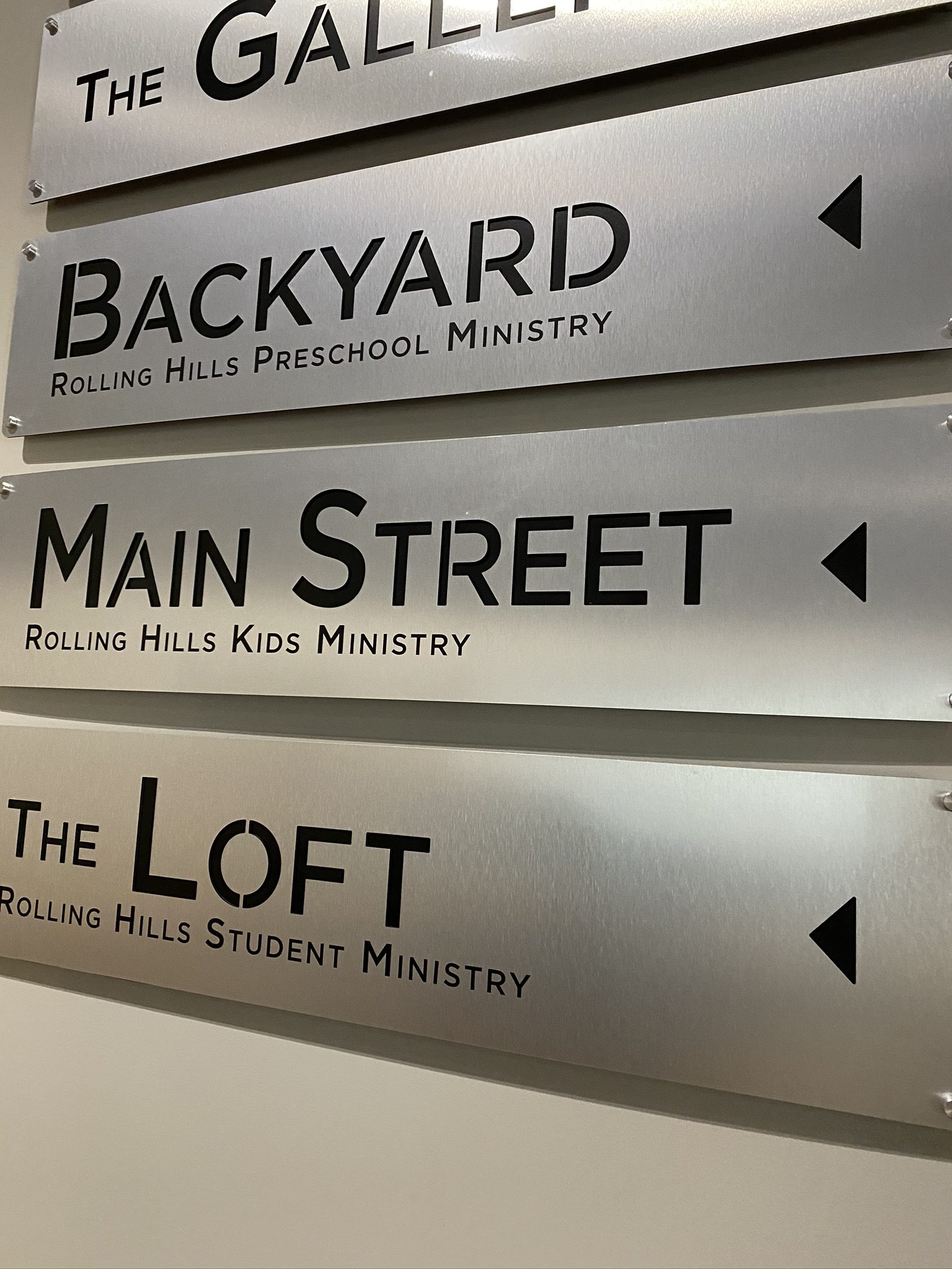 Brushed silver aluminum wayfinding signage with letters punched out to display a black background and mounted with silver stand offs.