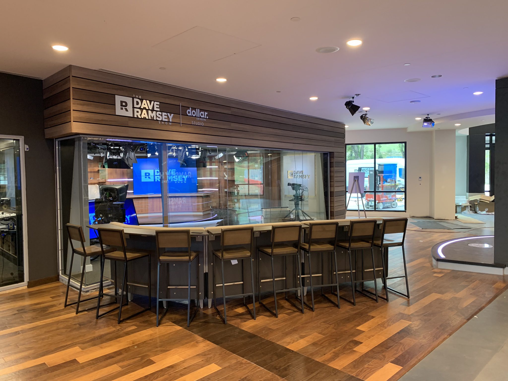 Modern studio with glass walls, "The Dave Ramsey Show" labeled, seating, lighting, cameras.