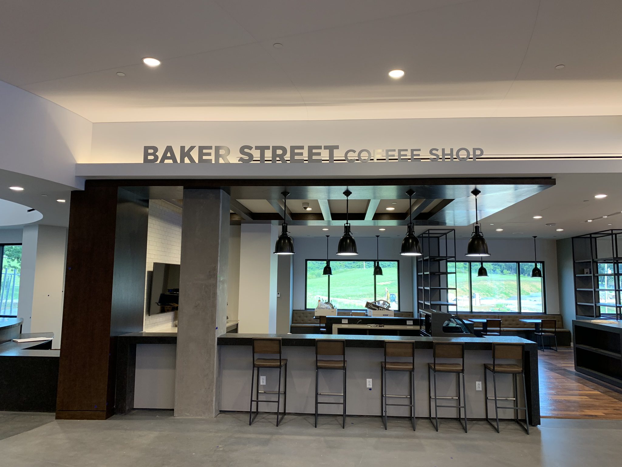 Modern coffee shop interior with high ceilings, bar stools, pendant lights, and large windows.